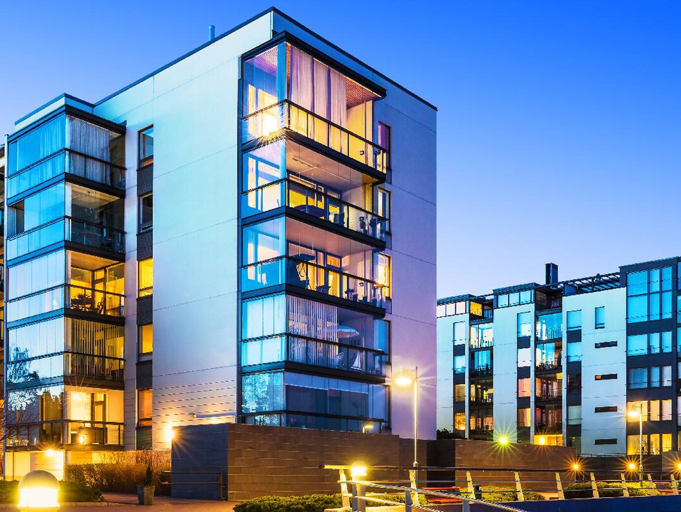 Exterior view of a large apartment complex, featuring large windows and balconies, with lights
