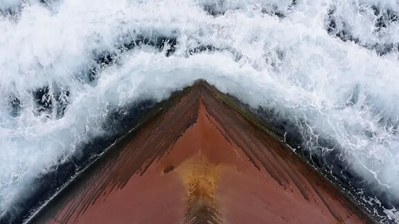 Ship’s bow cutting through ocean water with white foam.