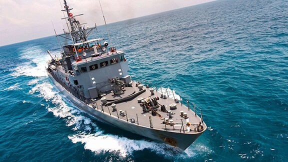 Military-style ship sailing through blue ocean.